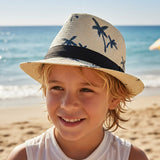 Child wearing a beige woven straw fedora with navy palm trees and a black band on a shore