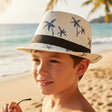 Boy wearing a white straw fedora sun hat with a navy palm tree print and black band