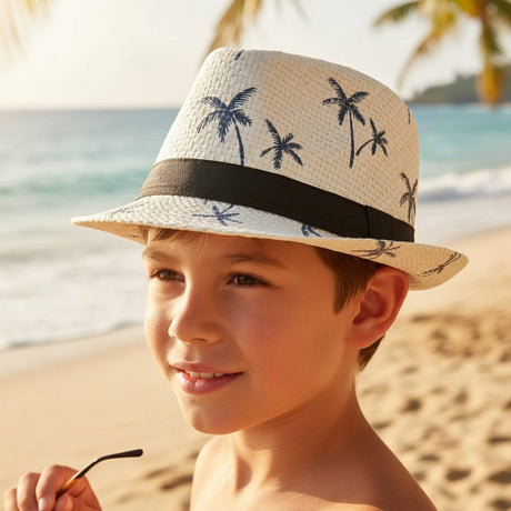 Boy wearing a white straw fedora sun hat with a navy palm tree print and black band