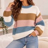 Woman in a chunky knit sweater with wide pastel pink, blue, camel and white stripes and jeans