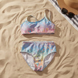 Pastel heart print bikini flat lay on sand with sunglasses