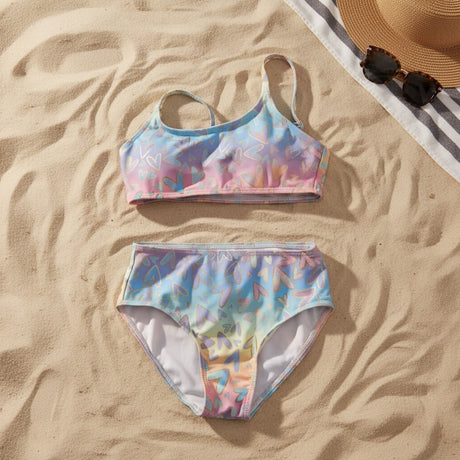 Pastel heart print bikini flat lay on sand with sunglasses