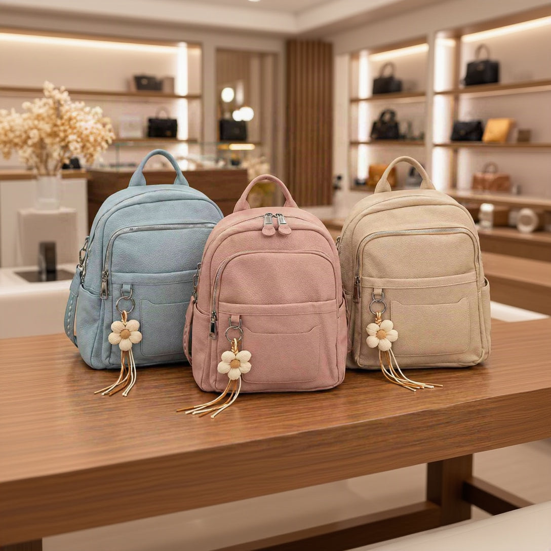 Light blue, pink and beige pebbled backpacks with cream flower charms lined up on a wooden counter