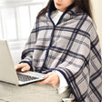 A person sitting with a laptop on their lap, covered with a grey and white checkered hoodie blanket.
