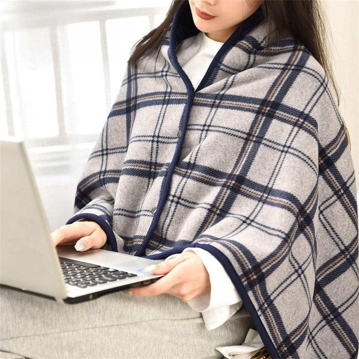 A person sitting with a laptop on their lap, covered with a grey and white checkered hoodie blanket.