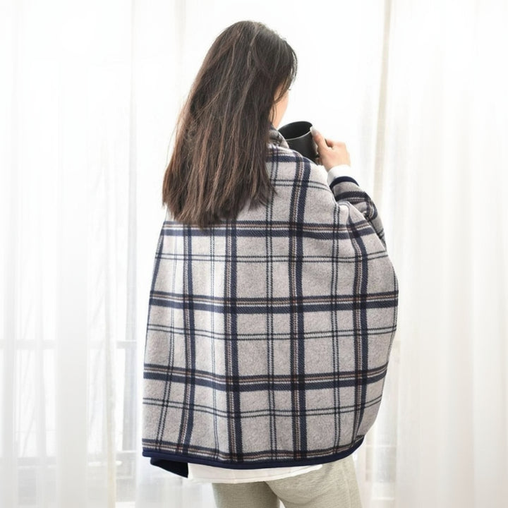 Person wrapped in a plaid blanket holding a mug against a white curtain background