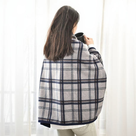 Person wrapped in a plaid blanket holding a mug against a white curtain background