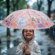 Girl in a hooded raincoat smiling under a peach umbrella printed with dolls and puppies