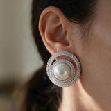 Silver spiral stud earring with a white pearl centre and baguette crystal rings worn on the ear