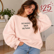 Woman in a pink sweatshirt with an All Money Back My Home slogan print and light blue jeans