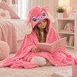 Child wrapped in a pink hooded Angel blanket with floppy ears, reading a book