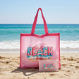 Pink tote bag with 'Beach Babe' text and a smaller pouch on a gray surface.