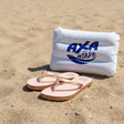 Inflatable pool float with 'AXLA Wake' branding on a sandy beach, accompanied by pink flip-flops.