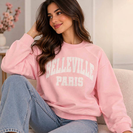 Smiling woman in a pink Belleville Paris sweatshirt with white varsity lettering