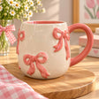Chunky pink ribbon bows stand out from a speckled cream barrel shaped mug