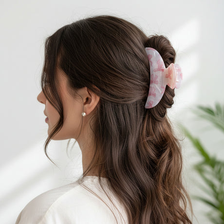 Pink bow print claw clip in a half up style beside a green plant