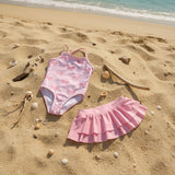 Pink bow stripe swimsuit and skirt flat lay on sand