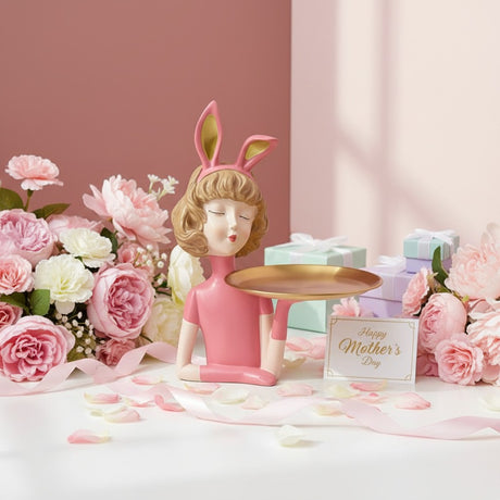 Coral bunny figure with her gold tray among peonies, petals and a mint gift box