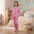 Young girl in pink pajamas standing in a bedroom with a bed and toys