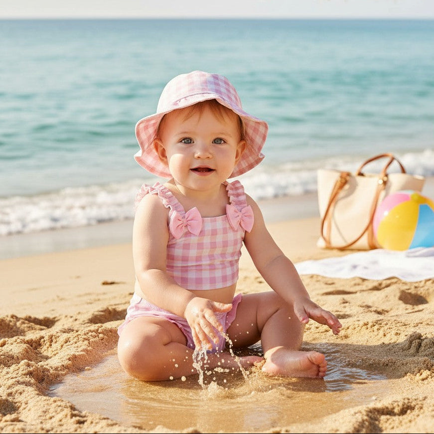 Baby wearing a pink checkered bow swimsuit with a matching bucket hat in the water