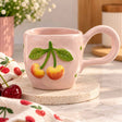 Golden yellow cherries and veined green leaves raised on a blush pink mug