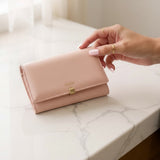 Pink wallet with gold clasp on a marble surface, hand reaching to open it