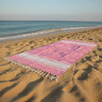 Soft pink striped beach towel with tassel edges on sandy beach with ocean waves