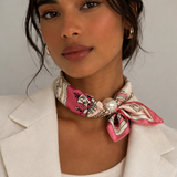Woman wearing a pink and white patterned foulard with a pearl accessory on a neutral background