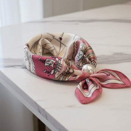 Pink and beige patterned foulard with a pearl on a marble surface