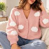 Pink knit cardigan with fluffy white cloud patches and matching buttons, worn sitting with jeans