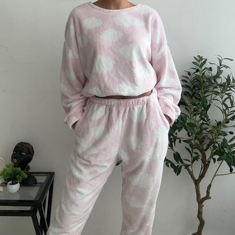 Pink cloud print fleece pyjama set worn standing by a plant