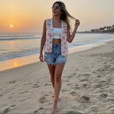 Woman walking on a beach at sunset with a floral vest and denim shorts.