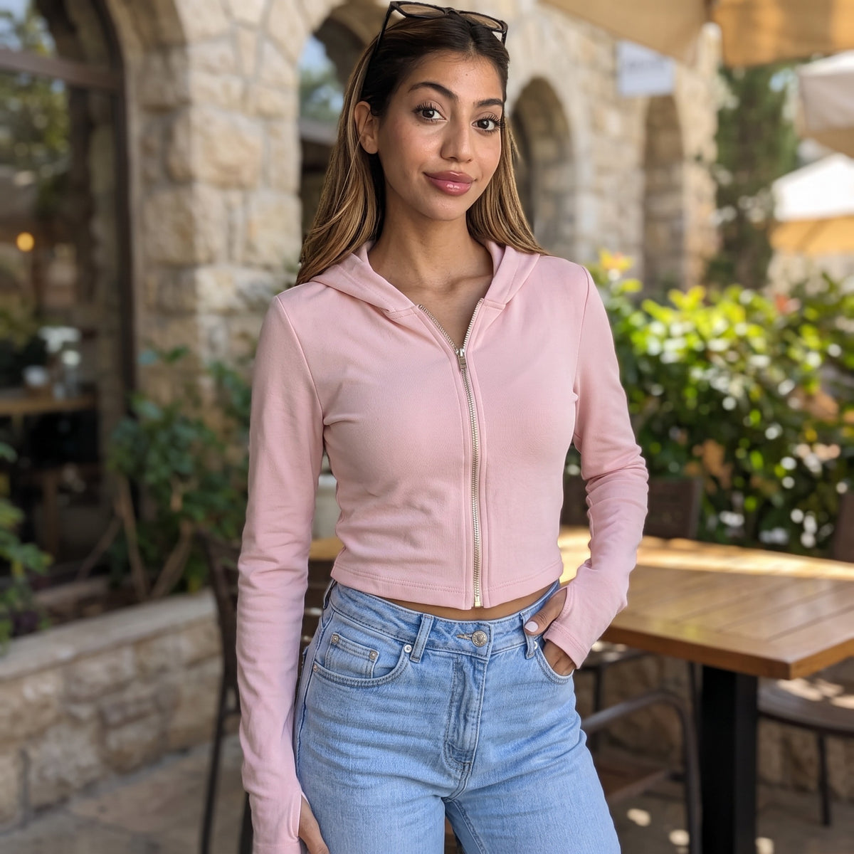 Woman in a soft pink cropped zip hoodie with long thumbhole sleeves at a cafe terrace