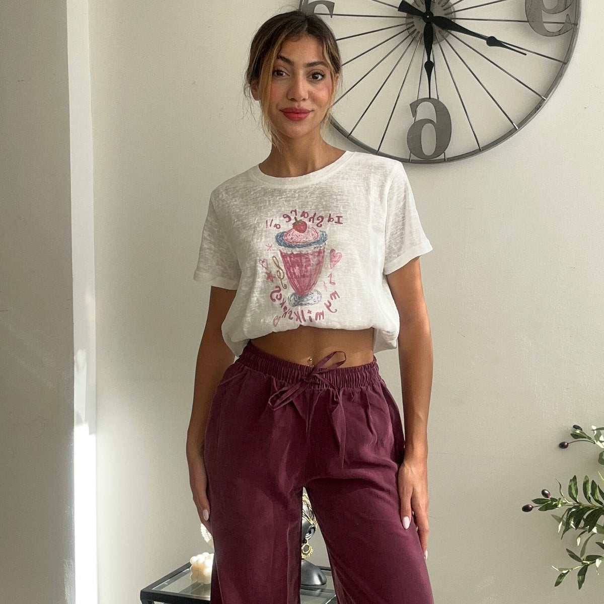 White crop tee with a pink drink print worn with burgundy wide leg trousers
