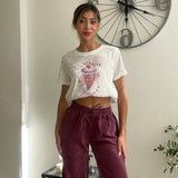 White crop tee with a pink drink print worn with burgundy wide leg trousers