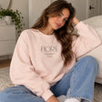 Woman in a pink crew neck sweatshirt with minimalist Fiore lettering, worn with light jeans
