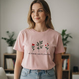 Woman wearing a pink tshirt with floral design and text in a room with plants and books