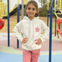 White hoodie with a pink daisy on the chest worn with pink joggers at a playground