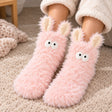 Woman wearing shaggy pink fluffy socks with upright bunny ears and big round eyes on a rug