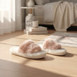 Pale pink faux fur cross strap slippers with a cream sole on a wooden floor