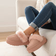 Person wearing pink slippers with fluffy trim sitting on a couch.