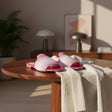 Pink woven handmade sandals on a wooden table with a cozy indoor setting