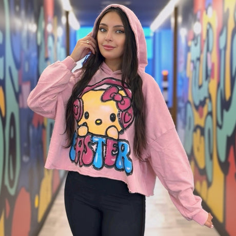 Person wearing a pink hoodie with a cartoon character of Hello Kitty and text in a colorful hallway
