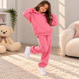 Girl in a hot pink fleece hoodie and matching joggers posing on one leg by a teddy bear