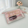 Pink case with 'KIND' text and hairbrush on a white surface with flowers in the background