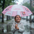 Smiling girl holding an open pink and white Huntrix print umbrella on a rainy street