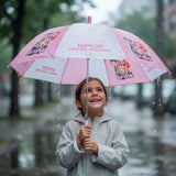Smiling girl holding an open pink and white Huntrix print umbrella on a rainy street