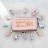 Pink pouch with 'KTMO' branding with measurements 13x25cm on a white background with hair accessories