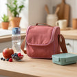 Pink insulated lunch bag on a wooden table with a water bottle, apples, and a snack container
