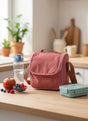 Pink insulated lunch bag on a wooden table with a water bottle, apples, and a snack container